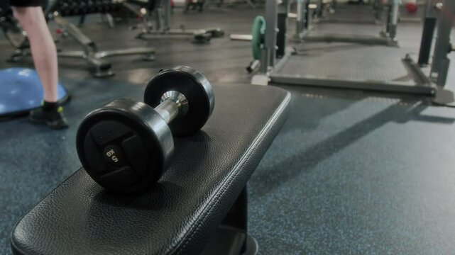 Close up shot of five kilo dumbbell resting on bench in gym, man exercising in blurred background