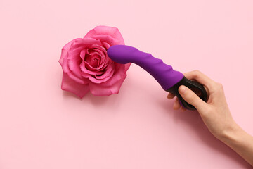 Female hand with vibrator and beautiful rose flower on pink background