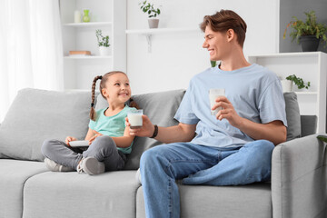 Obraz premium Little girl with cookies receiving glass of milk from her father at home