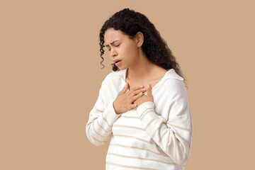 Young African-American woman having panic attack on beige background