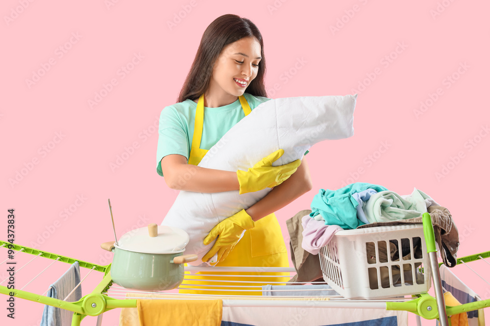 Wall mural overwhelmed asian mother with baby, cooking pot and clothes on dryer against pink background. multit