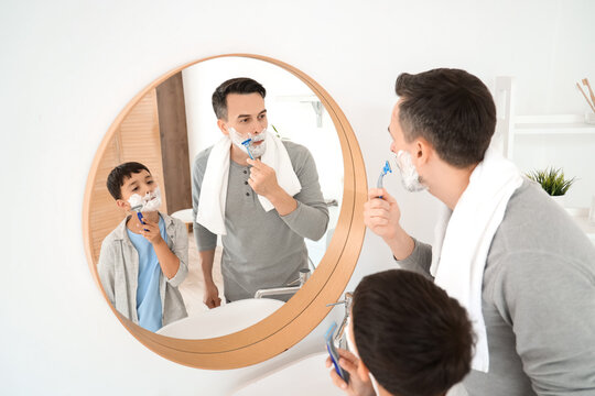 Happy father and his little son with foam on their faces shaving in bathroom