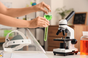 Teenage girl with chemical flasks, microscope and protective mask in room, closeup