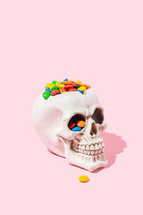 A human skull full of multicoloured sweets, pink background. Halloween idea,  trick or treat.
