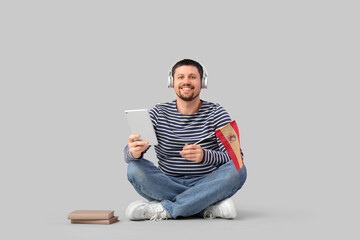 Handsome man in headphones with tablet computer and flag of Spain learning language online on light...