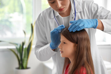 Naklejka premium Female doctor checking little girl's head for pediculosis in clinic, closeup