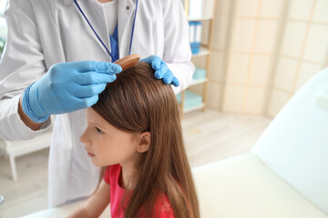 Female doctor combing little girl's hair in clinic, closeup. Pediculosis concept