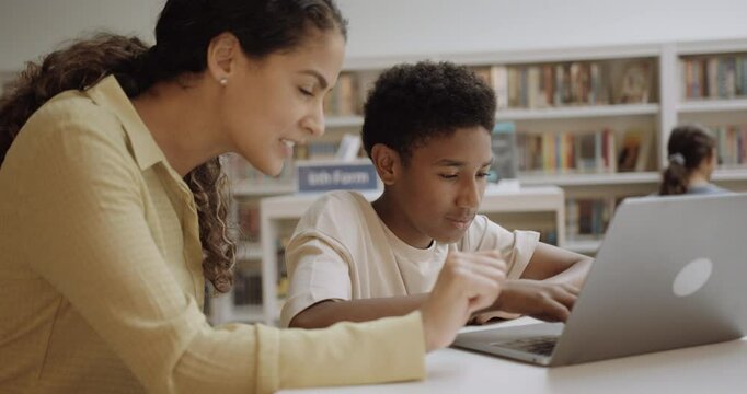 Teacher with School Child in Education Library using Laptop Technology