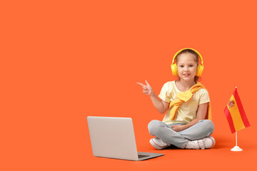 Little girl with Spanish flag and laptop pointing at something on orange background