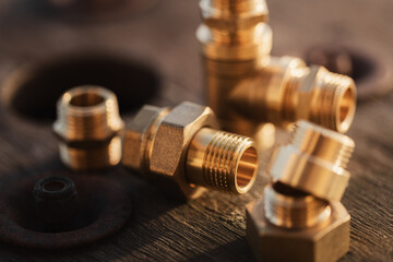 Brass plumbing fittings lying on a rustic wooden table on a sunny day (selective focus)