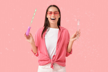 Young woman with soap bubbles wand on pink background