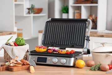 Basket and modern electric grill with vegetables on table in kitchen