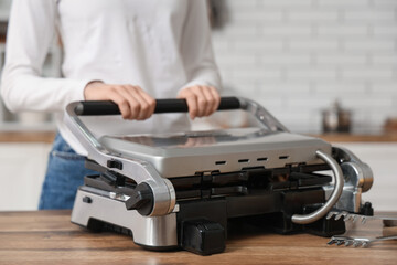 Woman closing modern electric grill on table in kitchen