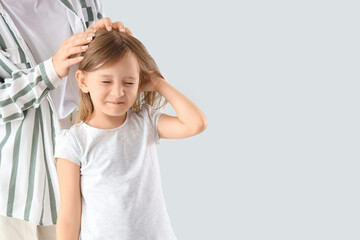 Mother checking her little daughter's head with pediculosis on light background