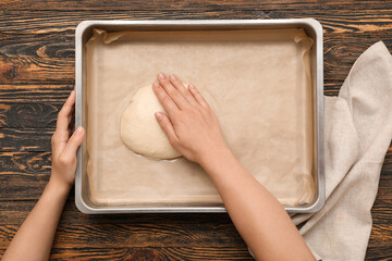 Female hands with baking tray and raw dough on wooden background, closeup