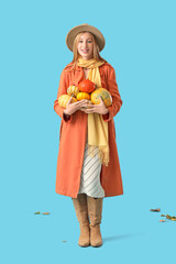 Beautiful young woman with fresh pumpkins on blue background