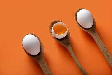 Wooden spoon with raw chicken eggs on orange background