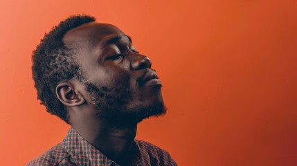 A contemplative man with eyes closed, set against a warm orange background, portrays a moment of introspection and inner peace.