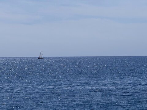 Blue ocean, clear sunny sky and sailboat on horizon.