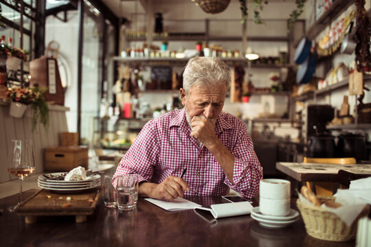Senior bistro owner writing notes after busy day