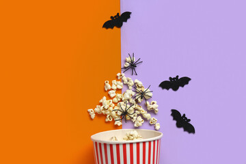 Bucket with tasty popcorn, bats and spiders for Halloween on color background