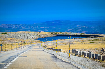 Vista panorâmica da Serra da Estrela, com seus imponentes picos rochosos, vastos campos verdes e céu claro, oferecendo uma paisagem tranquila e natural da maior montanha de Portugal.