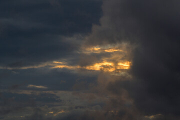 Sky with grey clouds and orange sun light at sunset in autumn