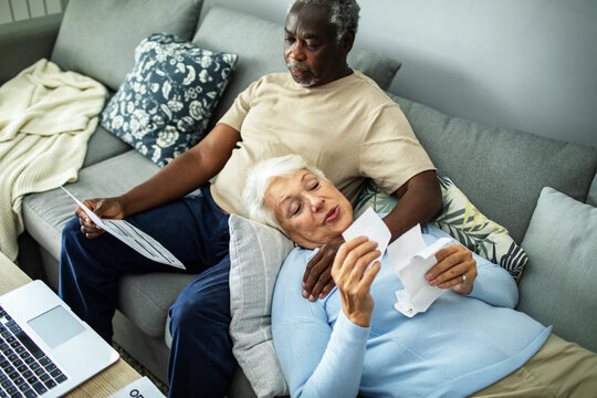 Diverse senior couple reading bills on the couch at home