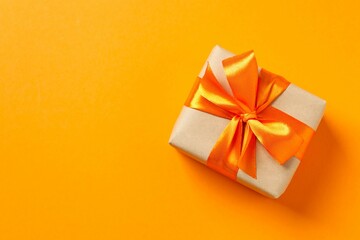 Top view photo of giftbox with orange satin ribbon bow on color background 