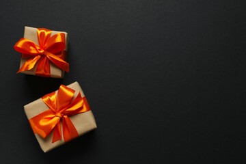Top view photo of giftboxes with orange satin ribbon bow on black background 