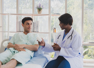 Obraz premium Patient caucasian man lying bed with woman doctor black people sitting carer physical therapist two person talk explain helping support explain medicine sick person inside clinic hospital room service