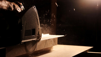 Close-up of a man cuts a wooden plank with an electric circular saw in a workshop. Cutting a piece of wood on a circular saw in backlight. Ideal topics related carpentry, efficient sawing techniques