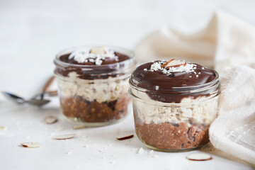 Two jars of homemade chocolate overnight oatmeal with shredded coconut and sliced almonds. Selective focus with blurred foreground and background. A joy to eat for breakfast or snack.