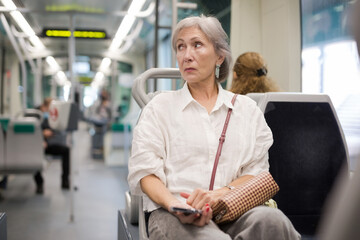 Mature woman with handbag sitting on seat inside tram.