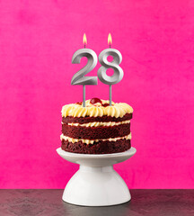 Birthday cake with number 28 candle - Red velvet on a fuchsia background.