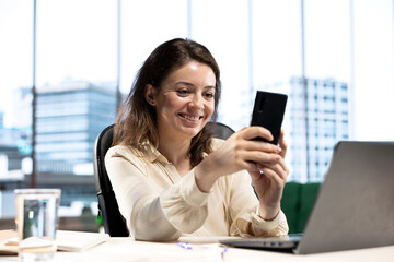 Young empowered business entrepreneur texting messages on her work break, feeling pleased with her career developments. Chatting with the employees for updates on the enterprise network.