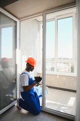 African handyman adjusting white pvc plastic window indoors. worker using screwdriver to repair upvc window.