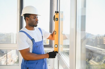 Workman in overalls installing or adjusting plastic windows in the living room at home