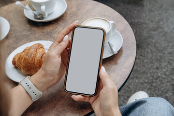 Mockup woman's hand holding using smart phone with white blank screen at coffee shop, mobile app design and advertising, online marketing