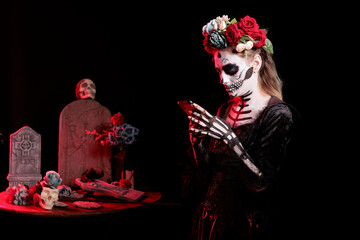 Girl texting friends on smartphone at Dia de los Muertes indigenous rites of honoring the dead. Woman checking social media on phone, participating at Day of the Dead in honor of the deceased