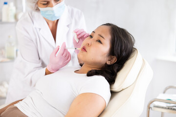 Closeup face of young female client receiving injections during lip enhancement procedure,...