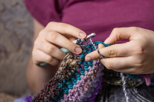 Young womans hands crochet colorful yarn with crocheting hook. Closeup details of handmade needlework art project and creative crafting techniques. Handmade textile artist nitting with yarn.