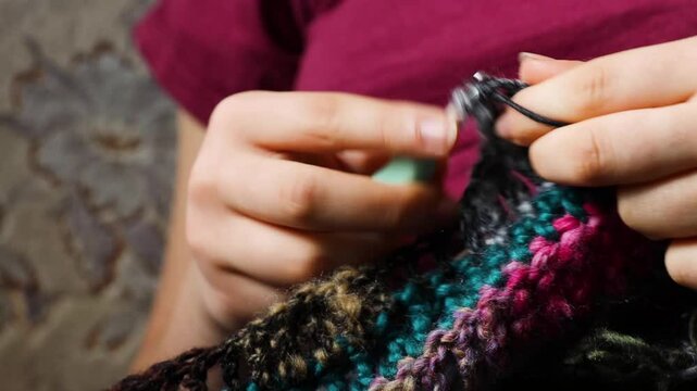 Young womans hands crochet colorful yarn with crocheting hook. Closeup details of handmade needlework art project and creative crafting techniques. Handmade textile artist nitting with yarn.
