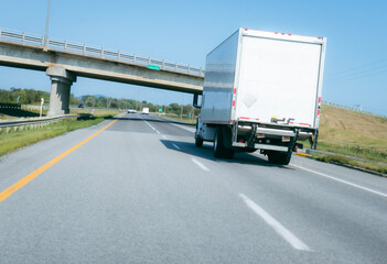 White truck driving towards an underpass on a two-lane highway view from the back.
