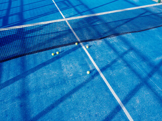 five balls near the net in a padel tennis court of blue artificial grass, aerial drone view