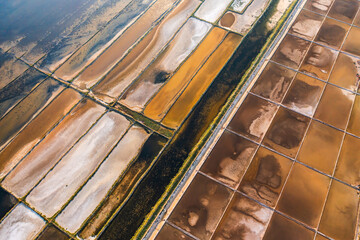 Aerial view of colorful salt pans with varied textures and patterns under bright sunlight. 