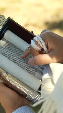 Close-up of Jewish Hands Holding Tzitzit While Reading a Torah Scroll. vertical