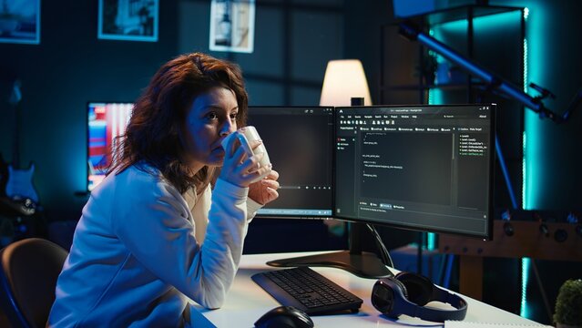 Portrait of smiling IT specialist drinking coffee while looking for company security vulnerabilities and preventing malware infections. Programmer enjoying hot beverage while writing code, camera B