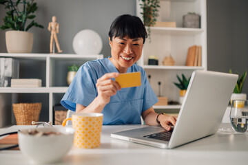 Asian female healthcare professional doing online transaction on laptop