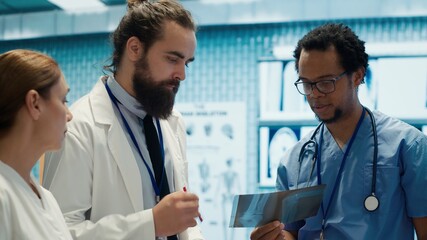 Hospital experts review x rays and discuss treatment plan strategy in research meeting. Doctors with expertise in radiology and disease prevention collaborate for insurance service. Camera A.